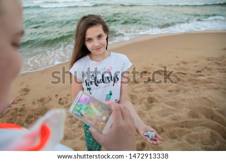 PORTRAIT OF SMILING HAPPY BRUNETTE GIRL SPENDING HOLIDAYS AT THE SEA WHILE STANDING ON THE BEACH AND POSING IN FRONT OF THE SMART PHONE