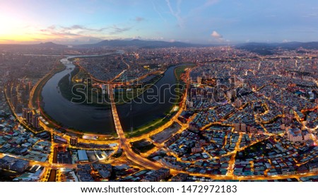 Aerial panorama of Taipei City embraced by rivers & mountains with Huazhong Bridge spanning Xindian River, the golden sun setting on the horizon & city lights of crisscrossing streets dazzling at dusk