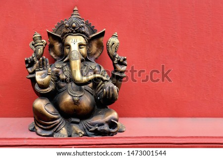 Bronze statuette of the Hindu God Ganesha on a red background with space for text. Indian Lord Ganpati.