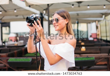 Young smiling woman takes pictures with a retro camera on the background of outdoor cafe