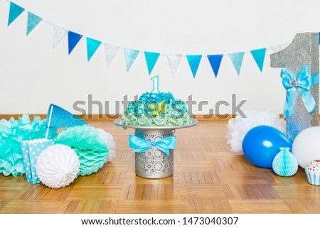 Festive background decoration for birthday celebration with gourmet cake, letters saying one and blue balloons in studio, cake smash first year concep