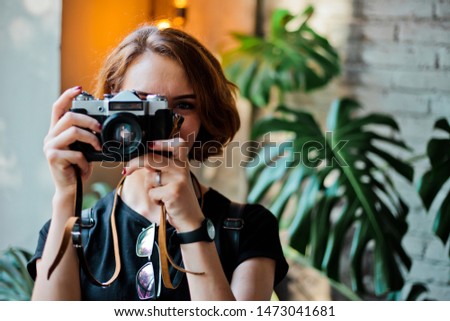 Portrait of a stylish hipster woman with a short haircut with retro camera takes a picture indoors