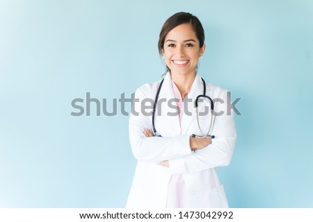 Smiling female doctor in lab coat with arms crossed against blue background Royalty-Free Stock Photo #1473042992