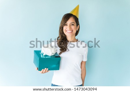 Excited beautiful woman with party hat holding birthday present over blue background