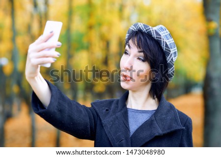 Beautiful woman taking selfie by smartphone and having fun in autumn city park, fall season, yellow leaves