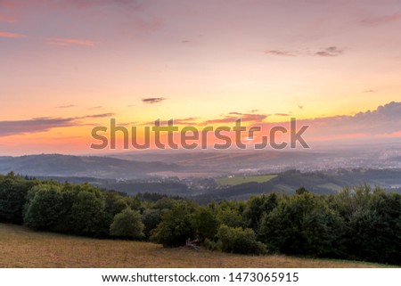 Sunset with view on landscape with fully colored clouds orange and purple and sun behind it and city Valasske Mezirici captured during summer late time.