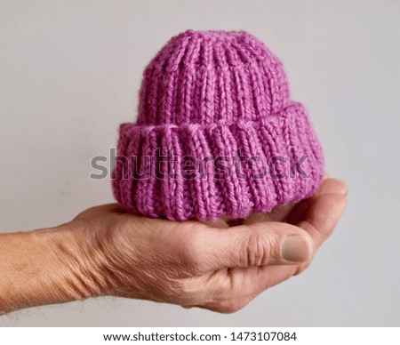 A man's hand cradles a small knit baby hat