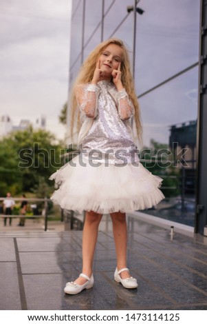 child girl blonde with long curly hair model in a pink puffy dress posing outdoors