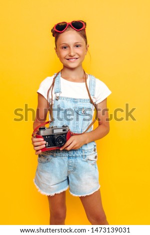 Attractive young girl, a teenager holds a camera in her hands and takes pictures on a yellow background