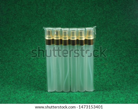A plastic pack of Glass bottle with golden spray cap on the green background. Perfume spray bottle. Packaging for liquid cosmetic or aroma. Sample of spray mock-up for branding.