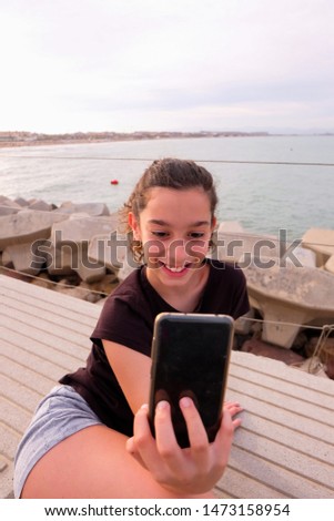 girl taking a picture with her cell phone near the beach