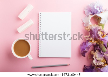 Purple and blue iris flowers and a cup of coffee with notebook on pastel pink background. Morninig, spring, fashion composition. Flat lay, top view.