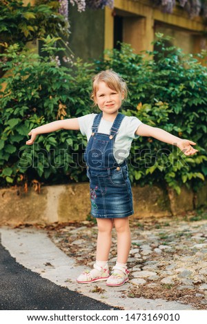 Outdoor portrait of cute little 3-4 year old girl, wearing denim pinafore