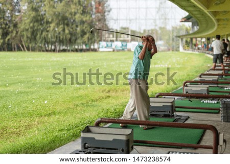 Senior man exercise practicing his golf swing at golf driving range.