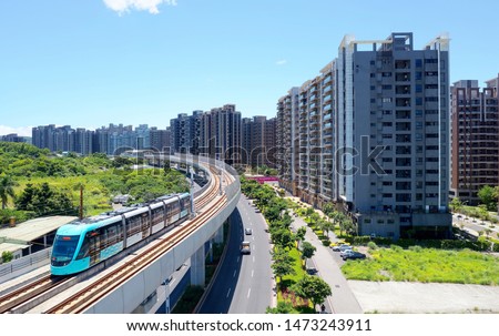 A metro train travels on the elevated track of Danhai Light Rail Transit System and residential towers stand next to the railway curve under blue sunny sky in Tamsui District, New Taipei City, Taiwan