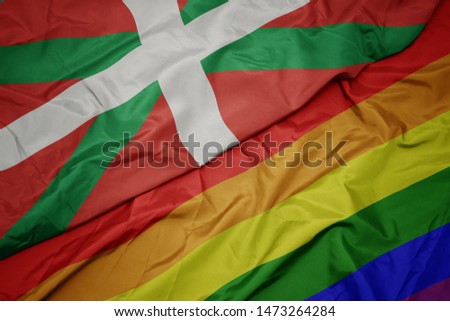 waving colorful gay rainbow flag and national flag of basque country.  