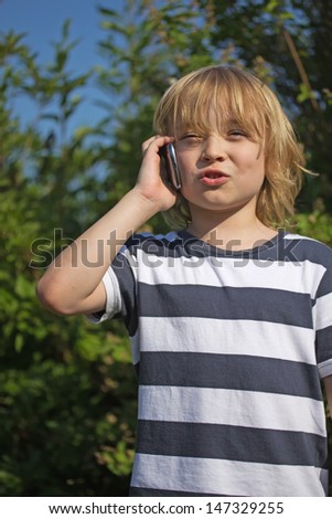 Young attractive blond boy dressed in a striped shirt is calling outdoors