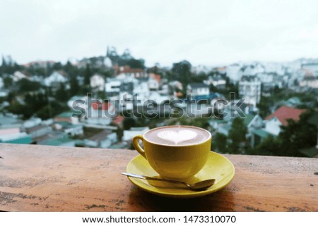 Close up a yellow coffee cup at balcony of a cafe and blurred sunset view of the city background, Cafe with view in Dalat of Vietnam, Brake time with a mug of coffee at morning on a blurred city view