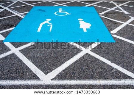 Icon sign indicating parking lane for elderly people, disabled person, and pregnant women only, painted in blue and white on asphalt road with traffic dividing lines.