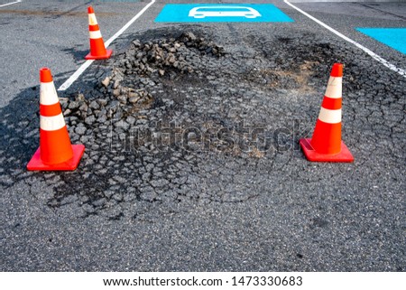 Vibrant orange and white traffic cones encircle damaged surface of asphalt road. Bus parking lane sign painted in blue and white.