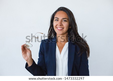 Content businesswoman holding eyeglasses. Beautiful young woman in formal wear holding spectacles and smiling at camera isolated on grey background. Business concept