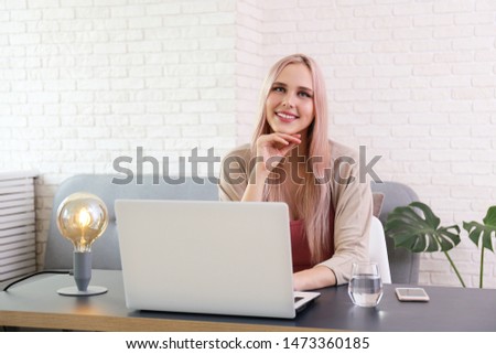 Young beautiful blonde woman with pink hair toner sitting in her workplace with white laptop. Portrait of teenage female model in corner office interior. Close up, copy space, background.
