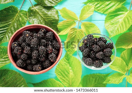 ripe blackberries in a large clay dish and a small transparent plate, on a blue wooden background, selective focusing, ingredients for fruit cocktails and yogurts