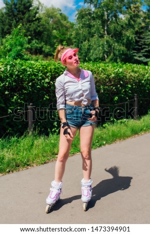 Portrait of an emotional beautiful young girl in a pink cap visor and protective gloves for rollerblades and skateboarding riding on rollerblades on the road.
