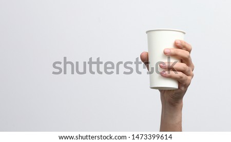 The man's hand is holding the white paper cup and up to the air isolated on white background, recycle, to go, zero waste concept. Royalty-Free Stock Photo #1473399614