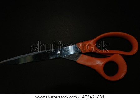 Scissors with orange plastic handles on a black background.