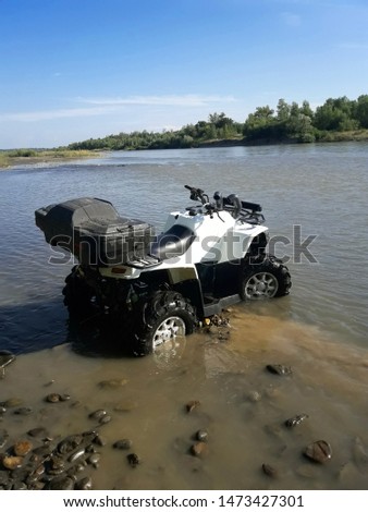 A white ATV stands on a sunny day by the river.