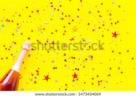 Champagne bottle with colorful party streamers for celebration on yellow background top view pattern
