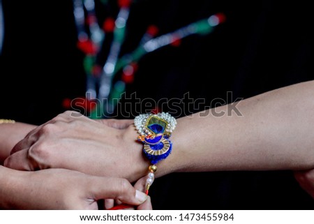 hand of a lady tying rakhi in hand of a guy during the hindu ritual of rakshabandhan with selective focus