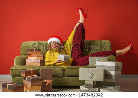 Beautiful young woman with Christmas gifts lying on sofa near color wall