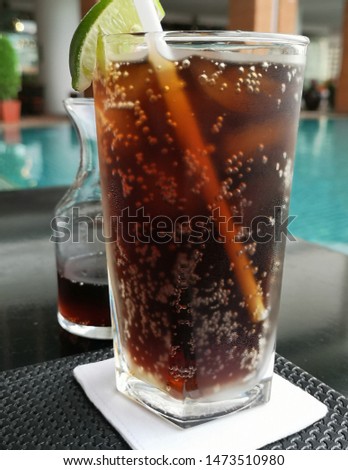 Cold drink in the glass on the table on the side of the swimming pool under the nice sunny day in Thailand.