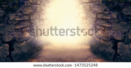 Mysterious fantasy photo background, magical trail leading out through stone dungeon cave walls towards mystical glow. Idyllic tranquil fantastic scene, empty road, way to fairytale, copy space.