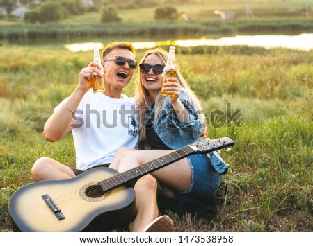 A couple in love with sunglasses drinking beer and enjoying the sunset.