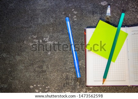 Pen and pencil lie on a notebook, view from the top. Self-adhesive paper for notation. Scissors and a ruler lie nearby. Top view on a black background, close-up
