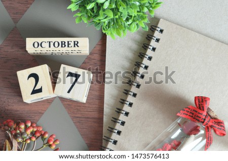 October 27. Date of October month. Number Cube with a flower, Rose bottle and notebook on Diamond wood table for the background.