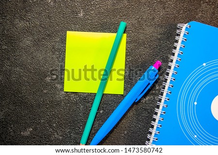 A blue notebook stunned with self-adhesive, a pen and a pencil lying next to it. View from above. On a black background
