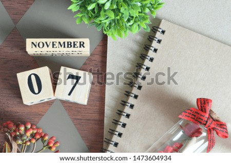 November 7. Date of November month. Number Cube with a flower, Rose bottle and notebook on Diamond wood table for the background.