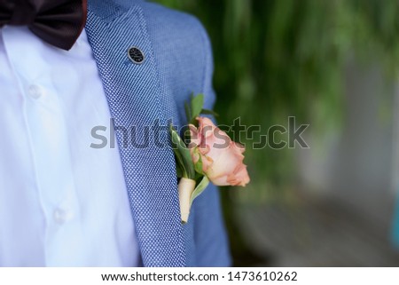 Groom, wearing light blue suit and white shirt with small flower rose living coral bouquet on chest. Close up picture of best man's boutonniere on wedding day.
