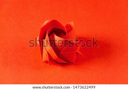 Red origami rose on red background. Japanese art of paper folding. Flat square sheet of paper transferred into a finished sculpture through folding and sculpting. Close up. Macro photo.