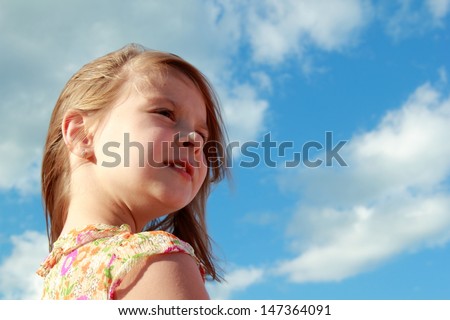 Portrait of cute smiling little girl on a background of blue sky with clouds outdoors