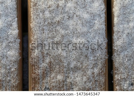 Surface of a wooden balcony floor with some fresh snow and ice on top of it. Closeup photo from a high angle. Photographed during winter season in Finland. Beautiful texture of the snowy surface!