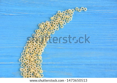Tiny round italian pasta with selective focus on blue textured wooden background. Uncooked noodles on wood backdrop. Raw organic vegetarian noodle. Small round rings pasta for soup. Food background 