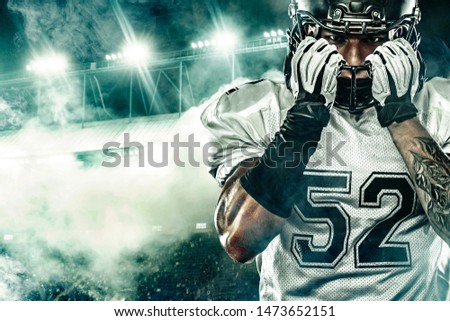 American football player. Sportsman with ball in helmet on stadium in action. Sport wallpaper. Closeup portrait.