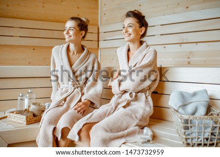 Two young beautiful girlfriends in bathrobes sitting together while relaxing in the luxury sauna Royalty-Free Stock Photo #1473732959