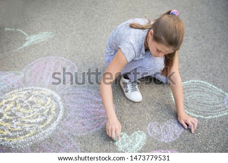 Girl drawing by chalk colorful pictures on the ground.