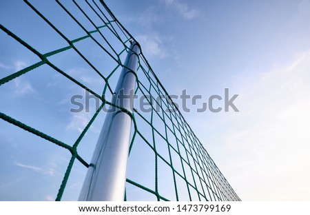 A silver colored pole with a net building a fence against the blue evening sky